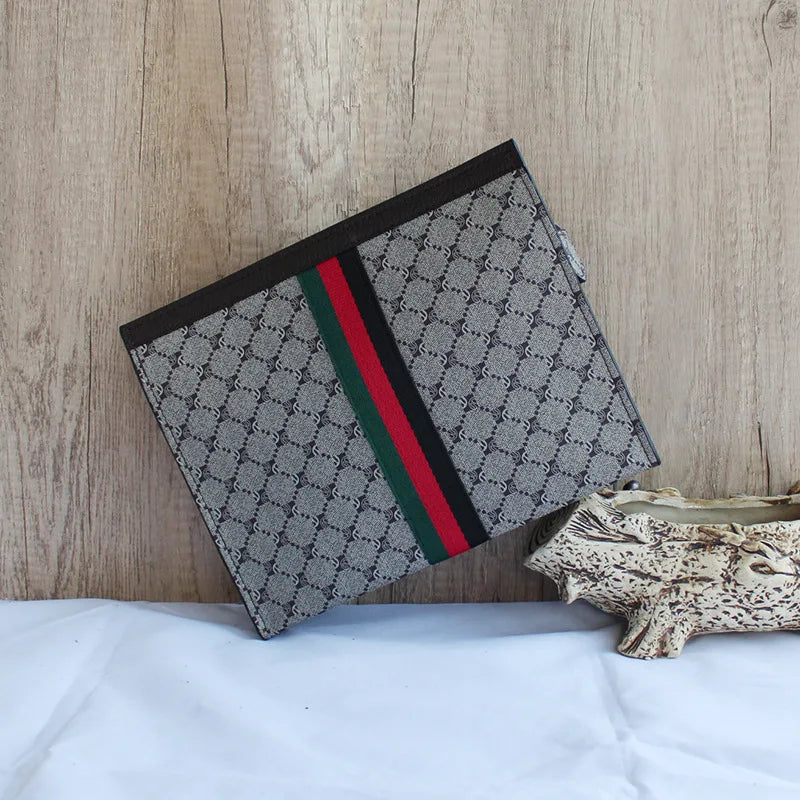 A black and gray designer clutch bag with green and red stripes resting on a light wooden surface.