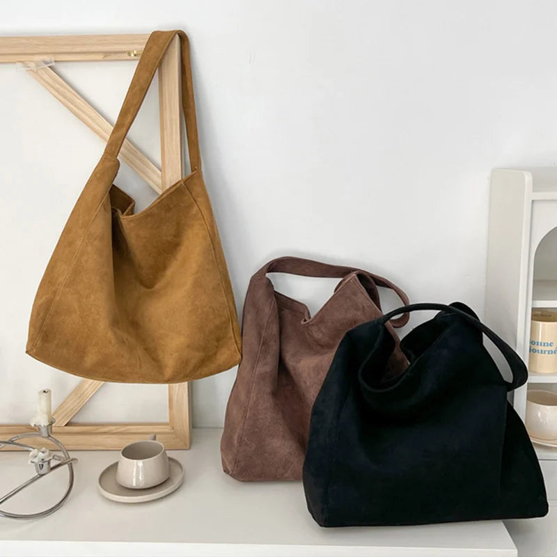 Three suede tote shoulder bags in brown, tan, and black displayed on a white surface.