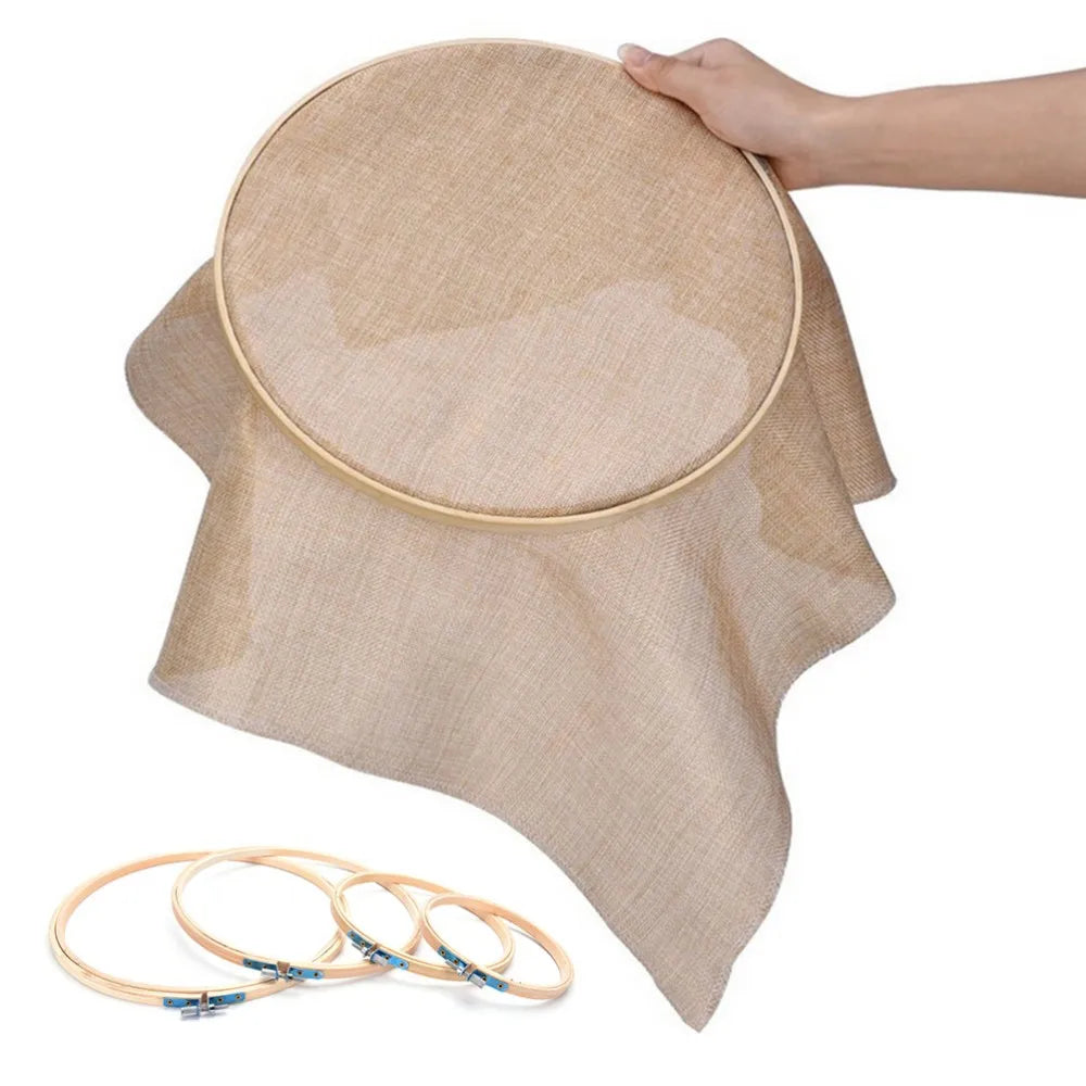 A hand is holding a beige bamboo embroidery hoop with an adjustable screw, showing the hoop's size and texture.