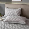 A stack of soft, quilted, light gray pillow protectors resting on a bed with a neutral headboard.