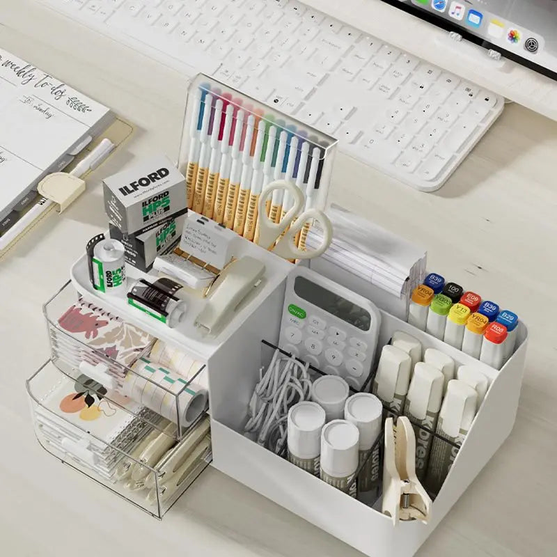A white desk organizer with transparent drawers holds various stationery items like pens, pencils, and rulers.