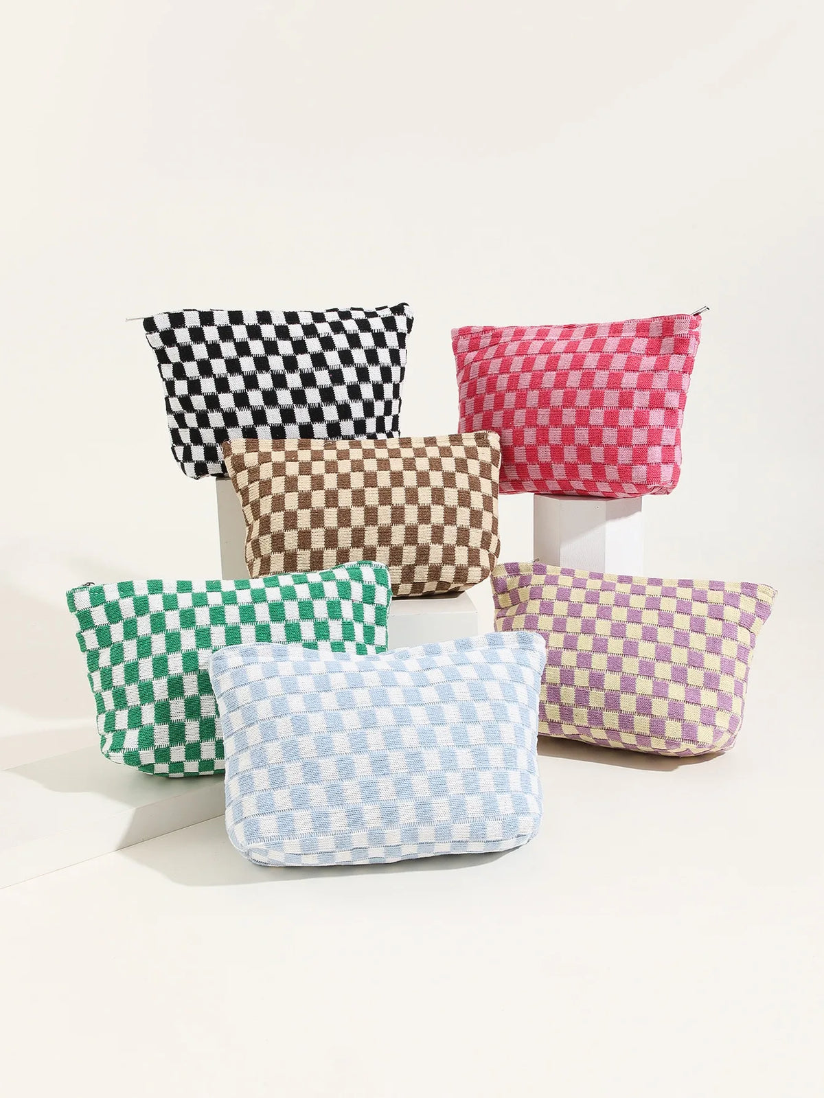 A collection of plaid fabric makeup bags in black, pink, brown, green, and purple are displayed on a white surface.