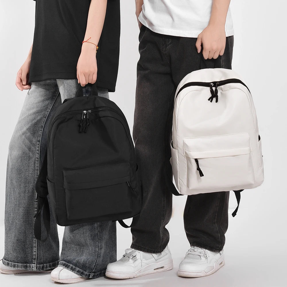 A person is holding a white minimalist canvas backpack with black accents and dark pants.