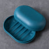 A teal portable soap dish with a lid is shown resting on a gray surface.