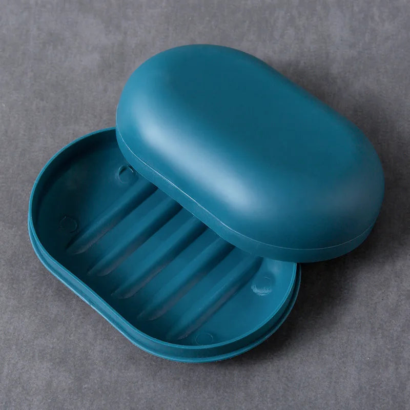 A teal portable soap dish with a lid is shown resting on a gray surface.