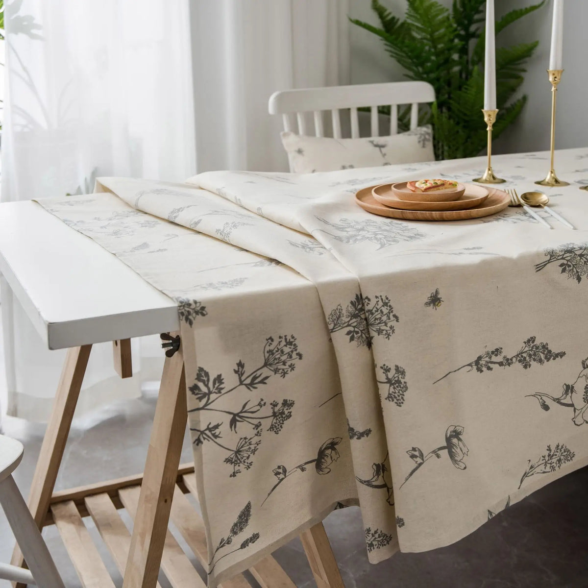 A beige cotton-linen tablecloth with a rustic fern print is displayed on a white wooden table.