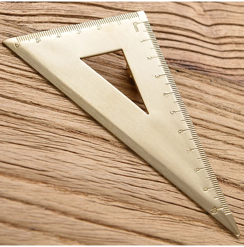 Messlatte aus Messing in Dreieckform mit Markierungen, diagonal auf einer Holzoberfläche liegend.