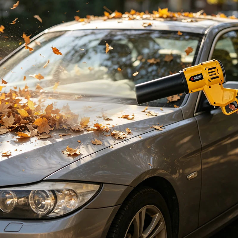 A yellow cordless blower and vacuum tool is blowing autumn leaves off a silver car's hood.