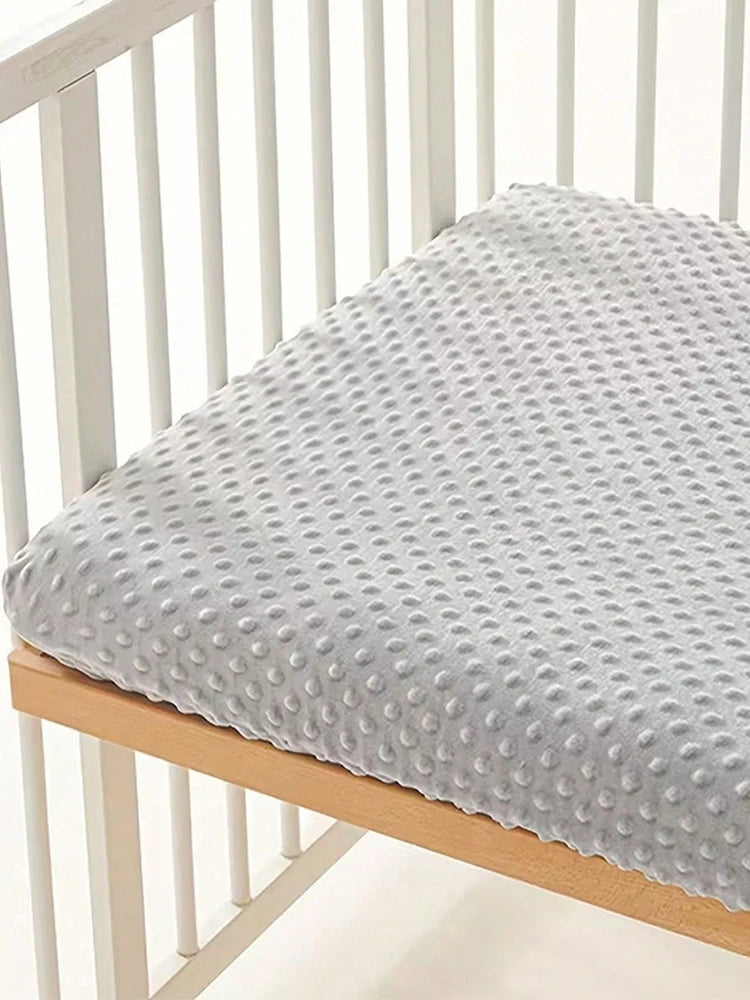 Housse de matelas en peluche texturée gris clair pour berceau ou lit, posée sur un cadre en bois.