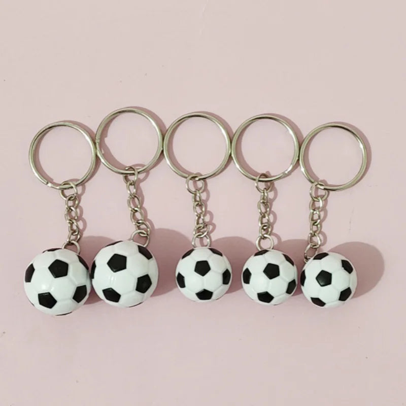 Cinco llaveros metálicos plateados con balones de fútbol negros y blancos.