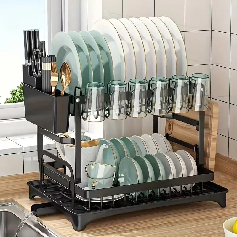 A black two-tier kitchen countertop drying rack holding stacks of white and green ceramic plates and glasses.