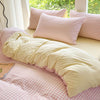 A pink and white gingham duvet cover set with two pillows on a bed near a window.