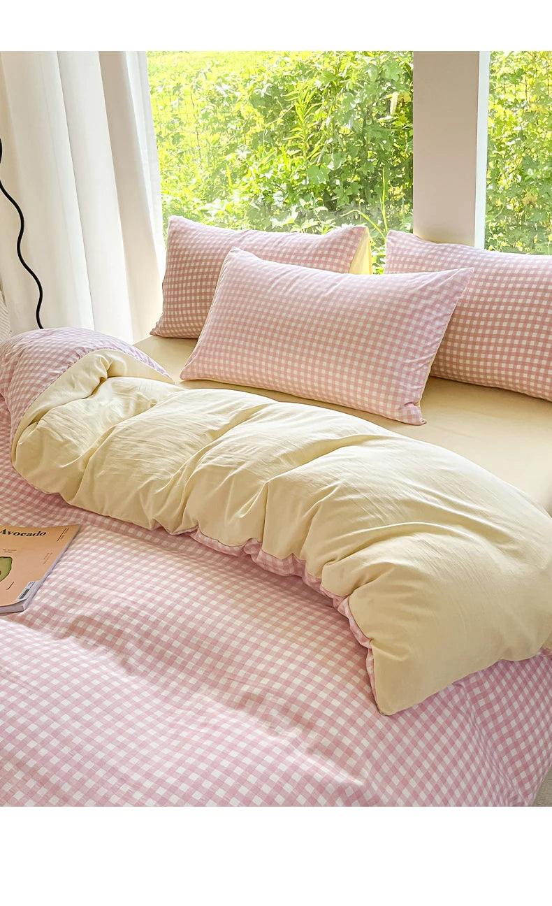 A pink and white gingham duvet cover set with two pillows on a bed near a window.