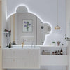 A modern bathroom vanity with a large mirror and white countertop featuring various skincare products.