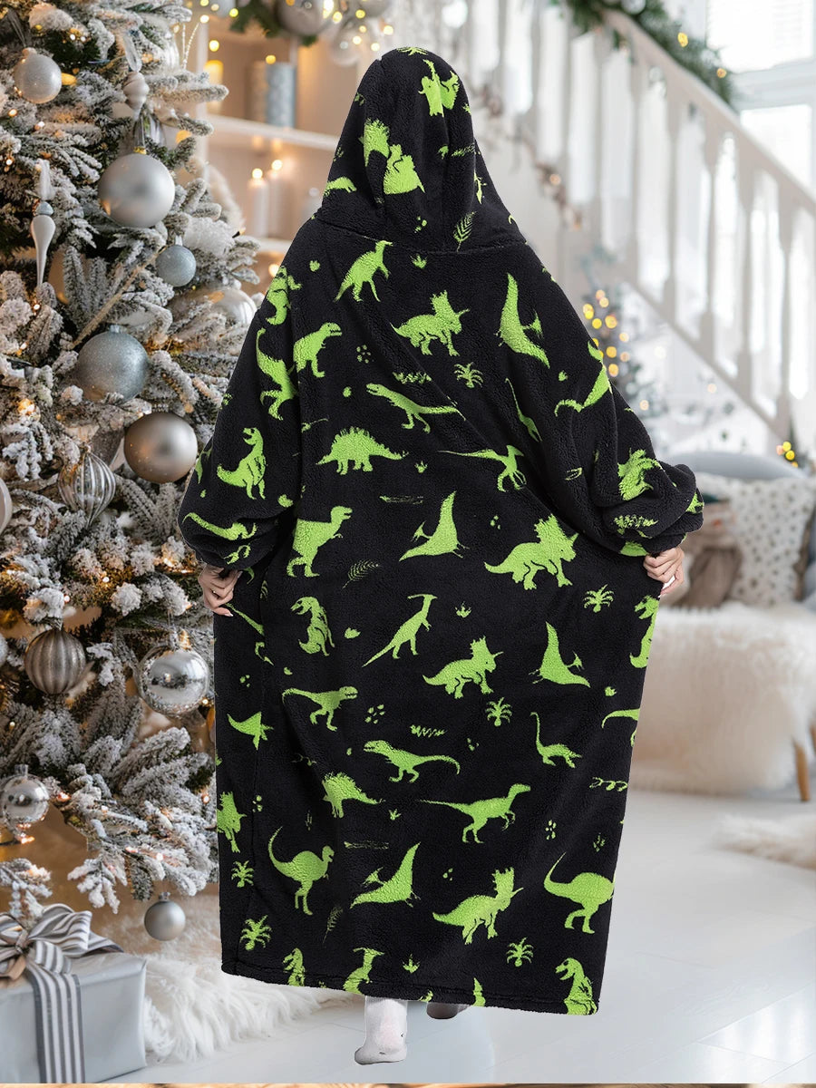 A person wearing an oversized black wearable blanket hoodie with a hood and sleeves stands in a bright indoor setting.