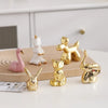 A collection of handcrafted ceramic elephant and rabbit jewelry holders in gold and pink colors on a white surface.