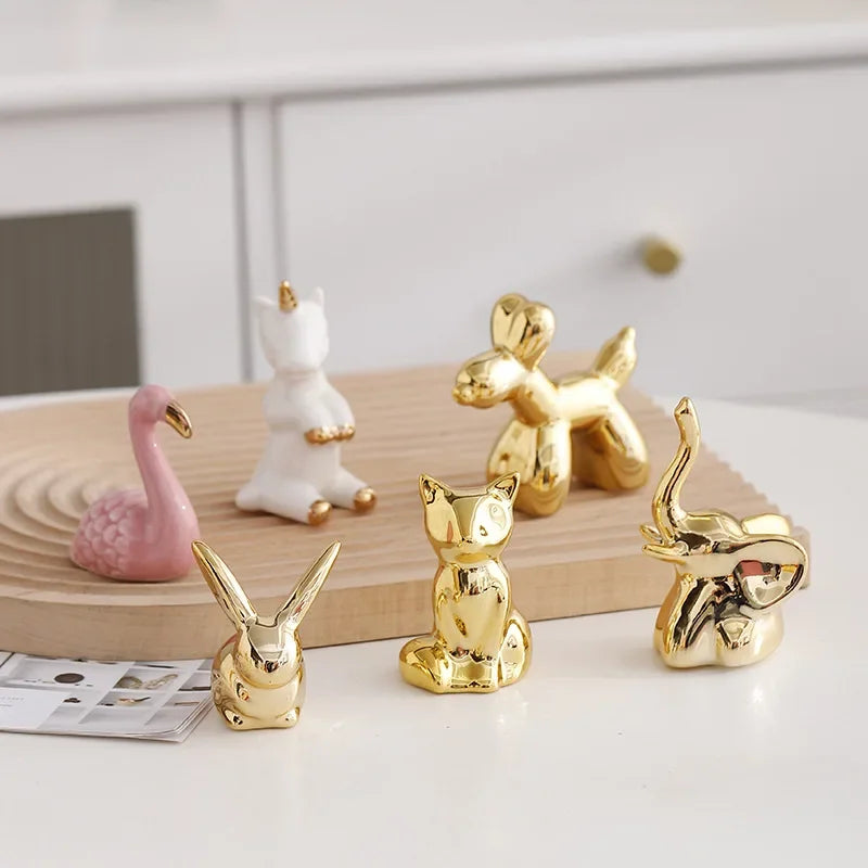 A collection of handcrafted ceramic elephant and rabbit jewelry holders in gold and pink colors on a white surface.