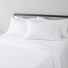 White microfiber bed sheet set with pillows and a dark headboard on a bed.
