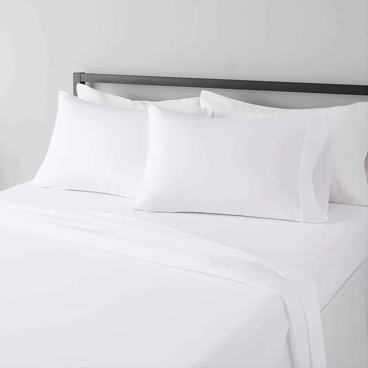 White microfiber bed sheet set with pillows and a dark headboard on a bed.