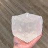 A hand holds a translucent, light pink frosted matte jumbo cheese stress ball against a blurred background.