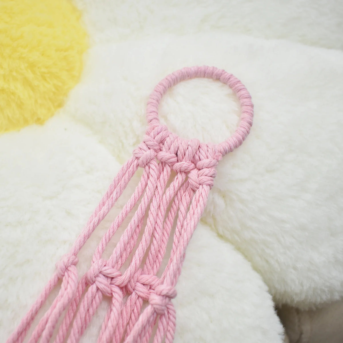 Pink handwoven net storage bag for corner toys with tassels on a white fluffy surface