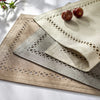A set of three square linen embroidered placemats in natural and gray tones with a small fruit on top.
