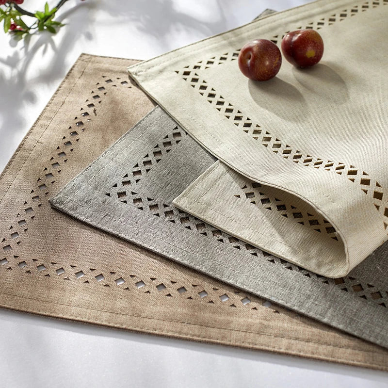 A set of three square linen embroidered placemats in natural and gray tones with a small fruit on top.