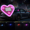 A dark sports car is illuminated by a large, glowing pink heart shape projected onto its hood and surrounding area.