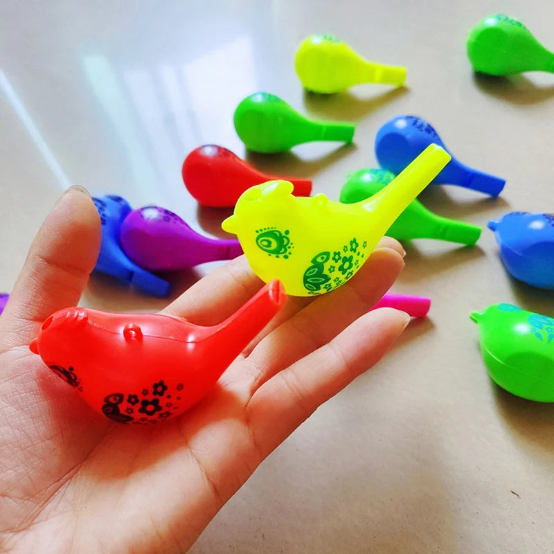 A hand holds a bright yellow plastic novelty bird whistle surrounded by various colored plastic whistles.