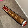 A rectangular brown accent mat with red lettering and carved designs lies on a gray carpet.