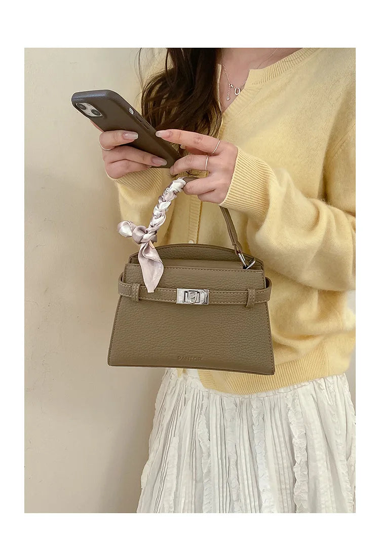 Eine Frau hält eine tanfarbene Kunstleder-Clutchtasche in der Hand vor einem hellen Hintergrund.