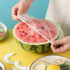 A hand is holding a slice of watermelon wrapped in a clear plastic bag on a yellow surface.