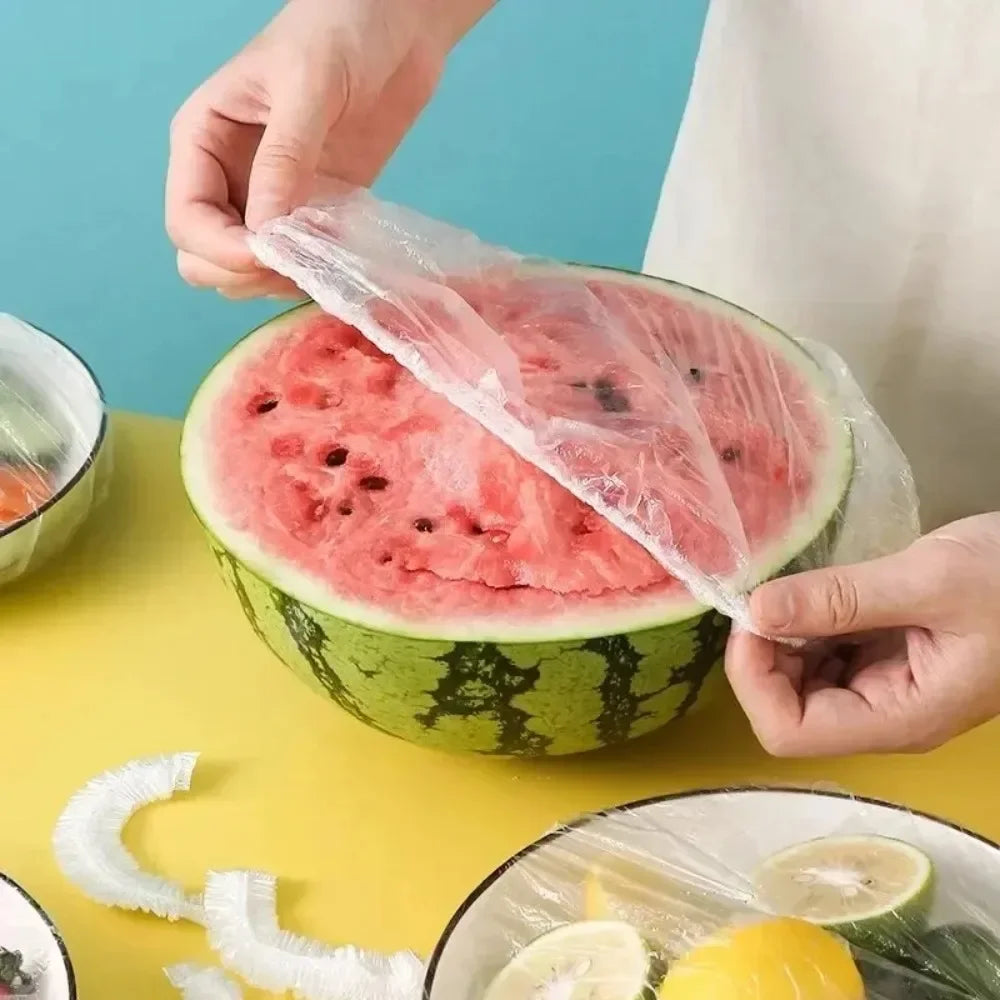 A hand is holding a slice of watermelon wrapped in a clear plastic bag on a yellow surface.
