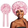 A woman models a pink satin silk sleep bonnet tied in a bow.