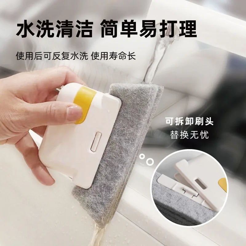 A hand is using a white multi-surface gap cleaning brush with a grey scouring pad to clean a window or glass surface.