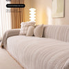 A beige jacquard anti-slip sofa cover with a herringbone pattern draped over a sofa in a bright, cozy living room.