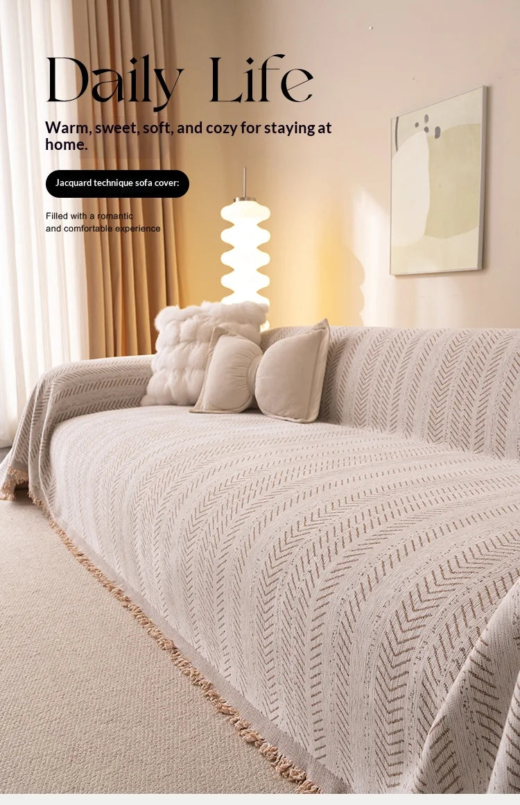 A beige jacquard anti-slip sofa cover with a herringbone pattern draped over a sofa in a bright, cozy living room.