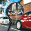 A close-up view through an adjustable wide-angle rearview mirror showing a white car in an urban street.