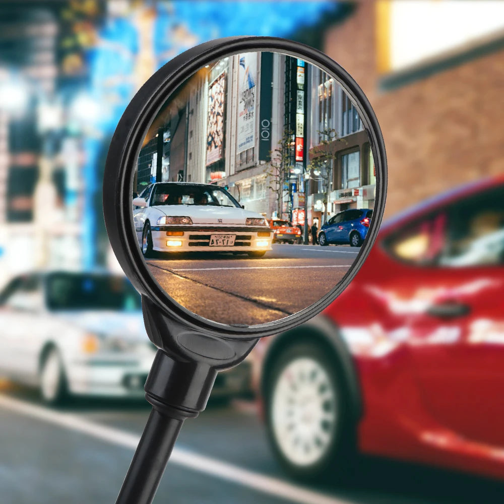 A close-up view through an adjustable wide-angle rearview mirror showing a white car in an urban street.