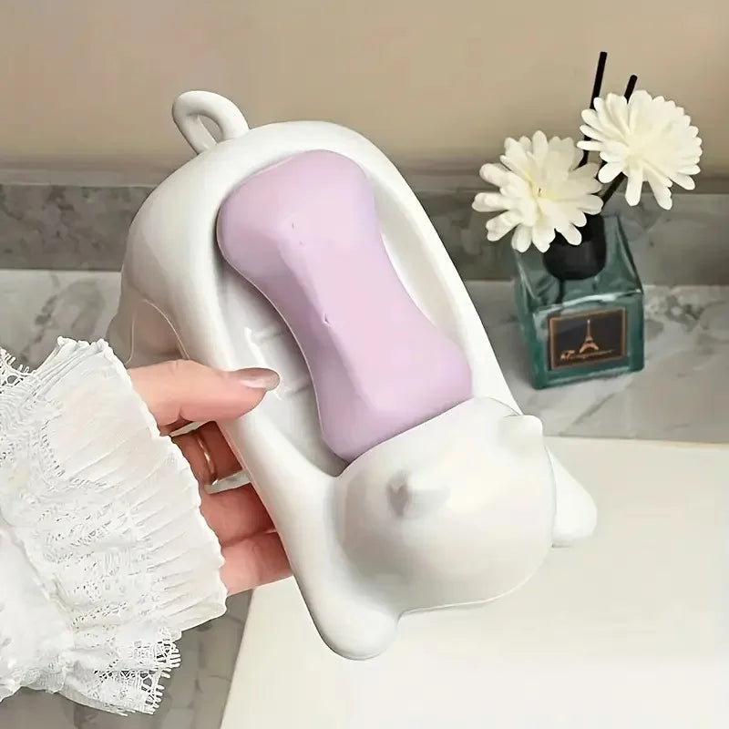 A hand holds a white cat-shaped soap dish with a purple bar of soap and a drainage tray.
