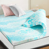 Un colchonero de espuma viscoelástica marmolado azul brillante y blanco, exhibido en una cama con almohadas rosa y gris.