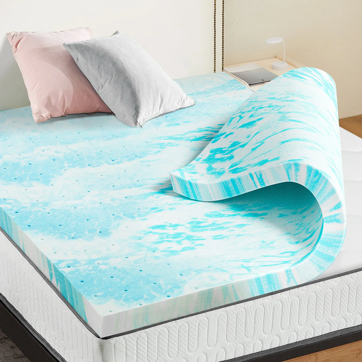 Un colchonero de espuma viscoelástica marmolado azul brillante y blanco, exhibido en una cama con almohadas rosa y gris.