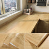 Roll of self-adhesive wood grain wallpaper showing natural light and texture on a wooden surface.
