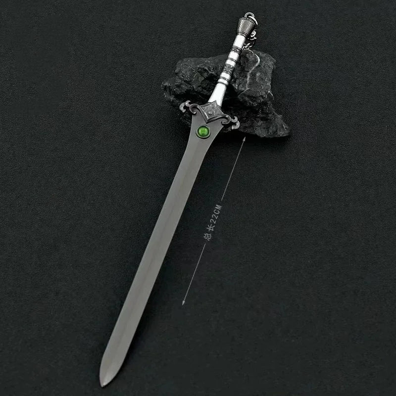 A detailed metal sword keychain featuring a blade, hilt, and a green ornament, resting on a dark rock.