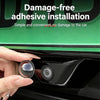 A hand installs a damage-free adhesive lens protector onto a car's rear view camera housing.