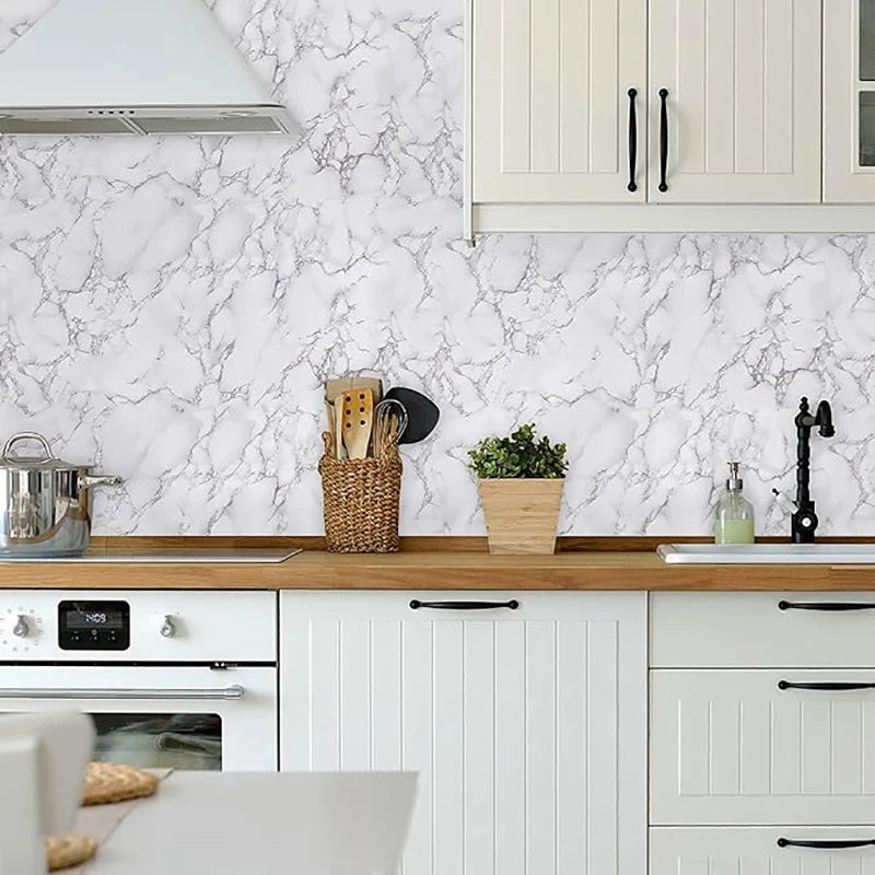 A kitchen cabinet and backsplash featuring white marble-patterned wallpaper and light wood countertops.