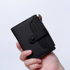 A hand holds a black premium PU leather bi-fold wallet with a zipper closure.