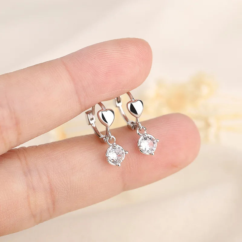 Una mano sostiene unos aretes de aro plateados con piedras de circonita cúbica.