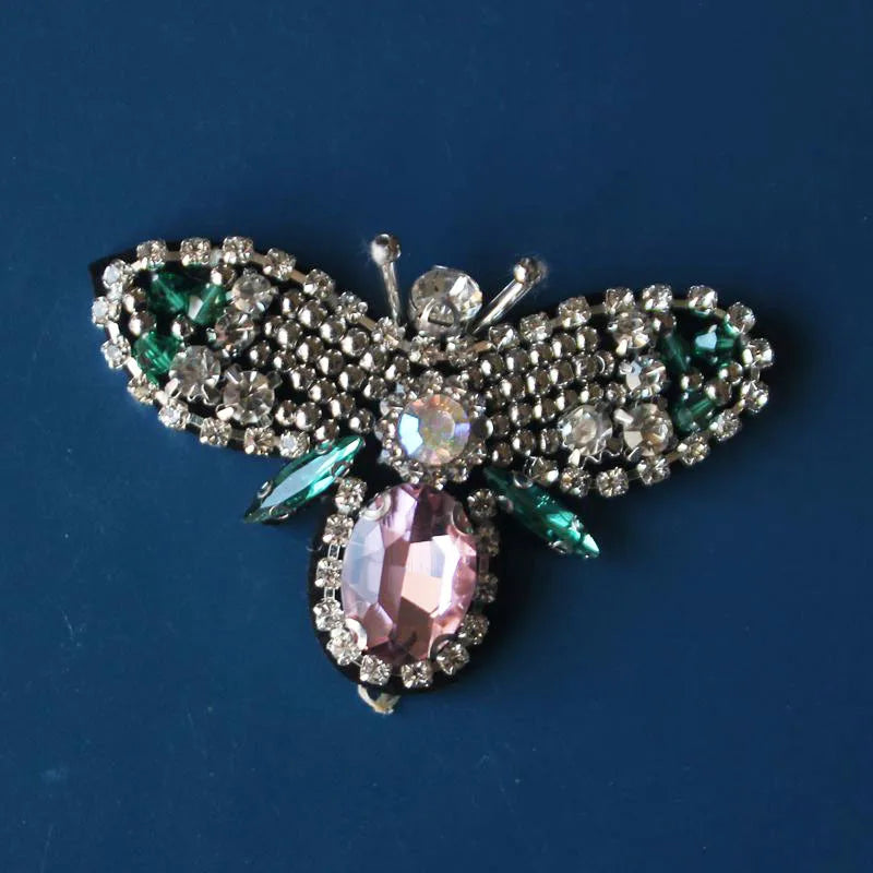 A handcrafted rhinestone bee sew-on patch featuring sparkling clear and pink stones on a green background.