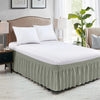 A white bed with a floor-length, pleated sage green wrap-around bed skirt and white pillows.
